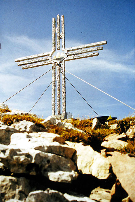 Siber glänzendes Gipfelkreuz vor blauem Himmel