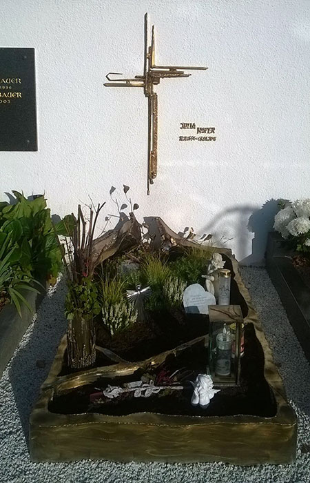 Modernes Grabmal mit einem Kreuz an der Wand und einer individuellen Einfassung