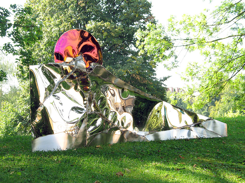 In dieser Gartenskulptur spiegelt sich die grüne Wiese im polierten Blech. Eine rote Scheibe aus Edelstahl schaffte einen interessanten Kontrast.