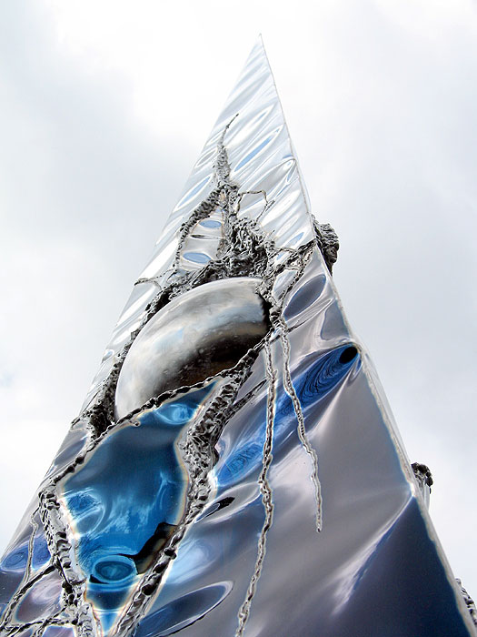 Welded metal sculpture with a blue and a mirror polished surface. This sculpture is standing in a garden